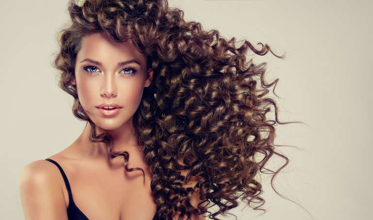 Young, brown haired woman  with voluminous hair. Beautiful model with long, dense and curly hairstyle and vivid make-up.Tensed, spring-like curls on the hair.Incredibly dense, wavy,and shiny hair.
